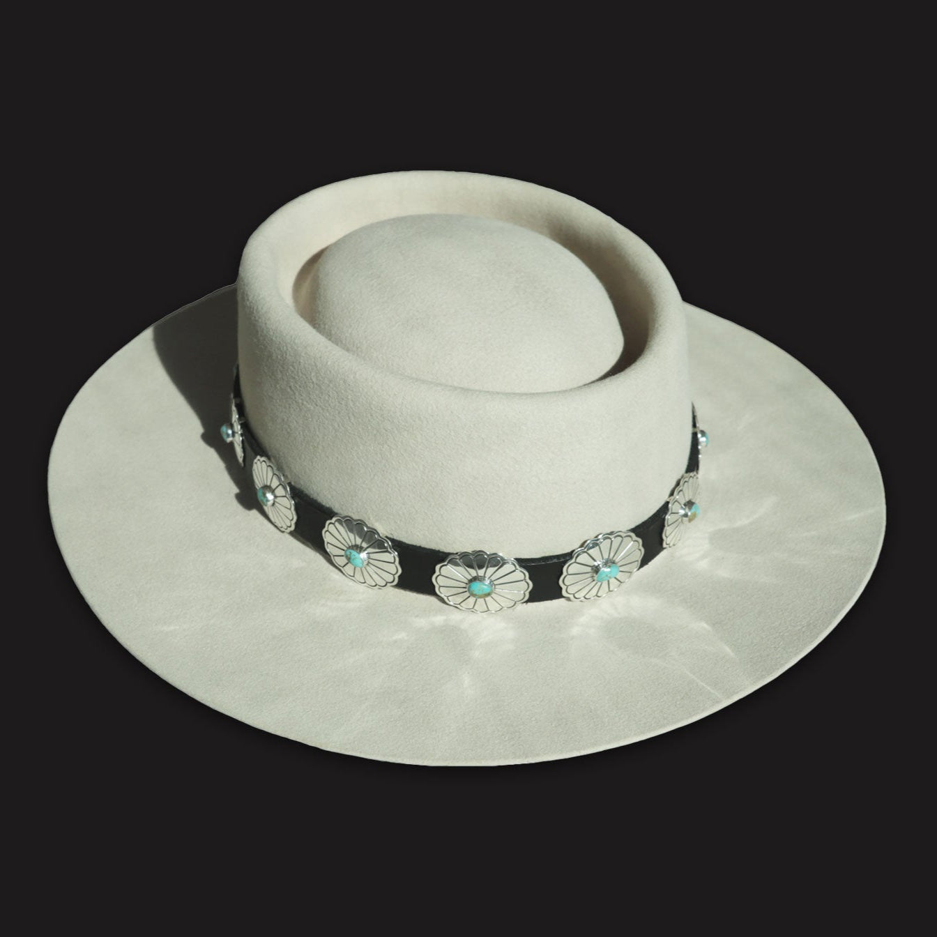 Rough Rider hatband: Stamped silver conchos with turquoise centers on a dark leather band, shown on a light felt Montana Territory Hat.