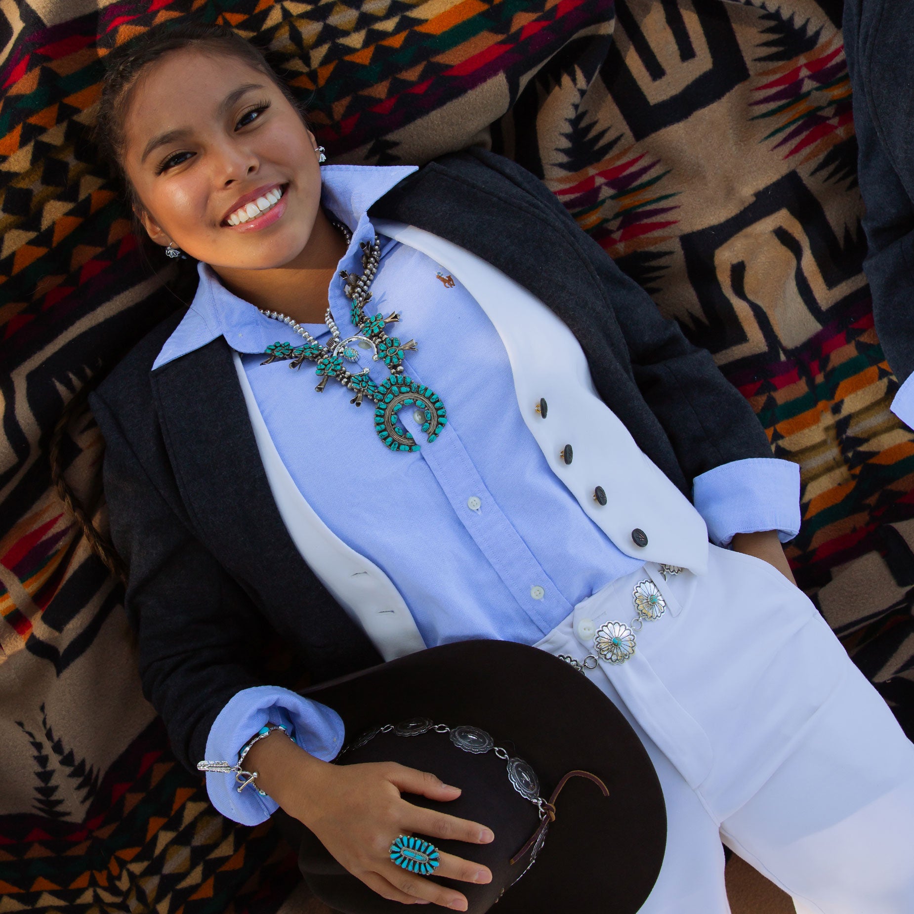 Woman wearing a grey wool coat with white vest, blue shirt, and turquoise jewelry on a pendleton blanket.