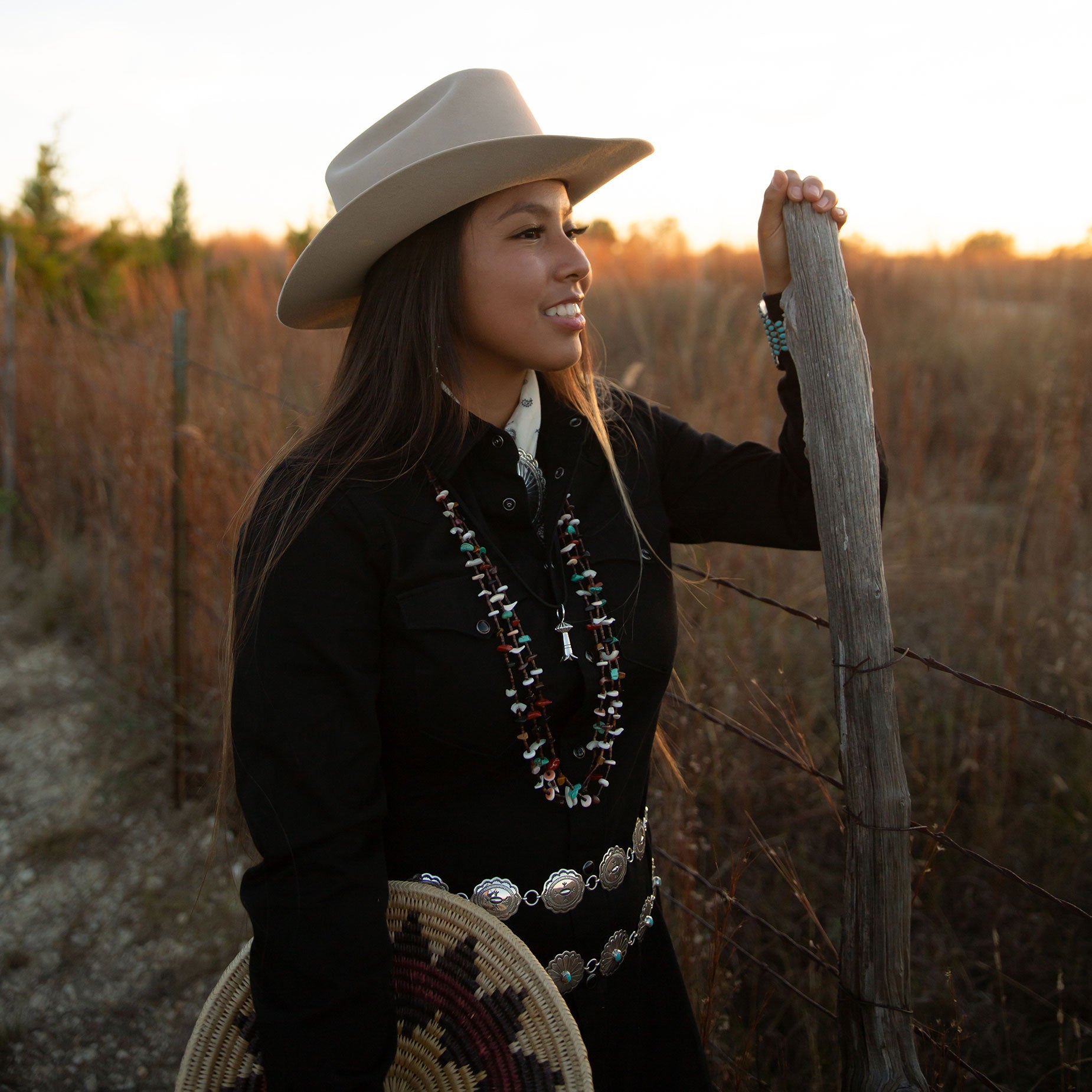 Woman in navajo sterling silver jewelry by Cowgirls & Indians holding a navajo wedding basket at sunset on a texas ranch