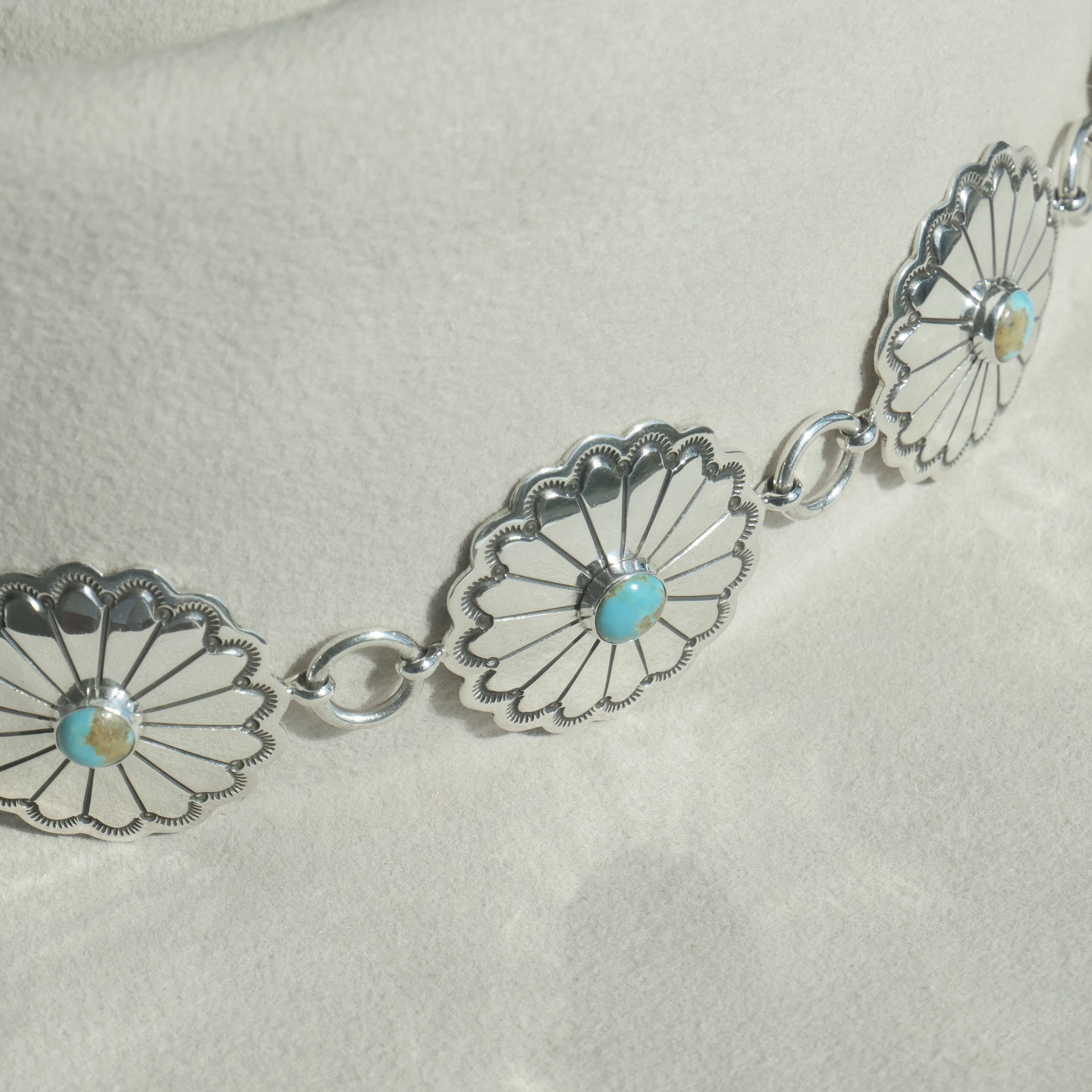 Detailed shot highlighting the intricate stampwork and central turquoise set in a sterling silver concho of the Nizhoni Navajo hatband.