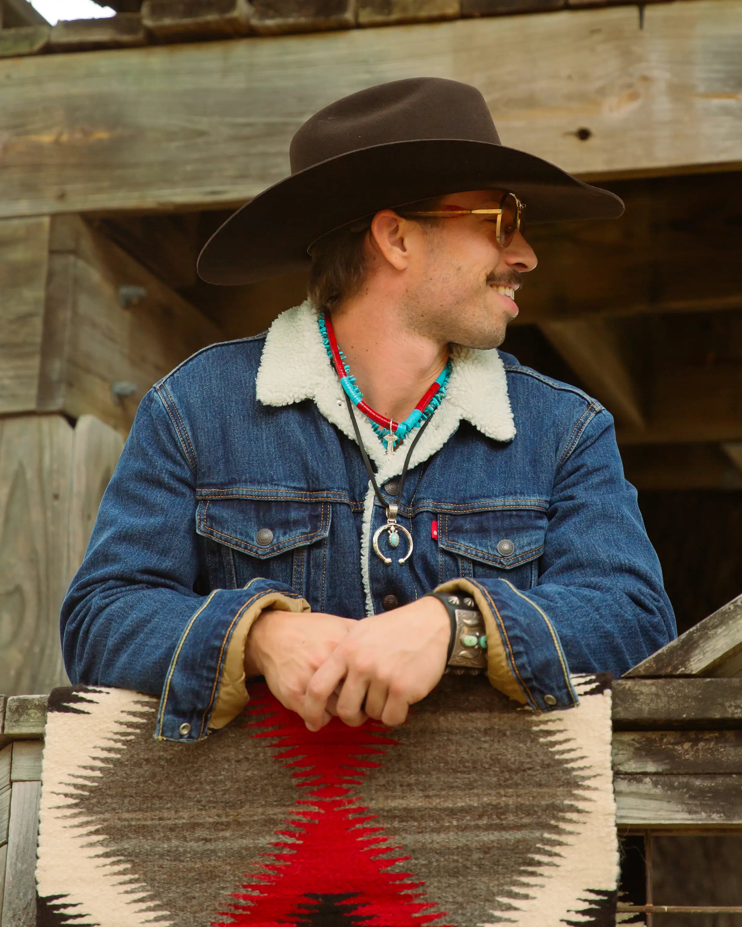 Man wearing a cowboy hat and denim jacket holding a eyedazzler navajo rug outdoors