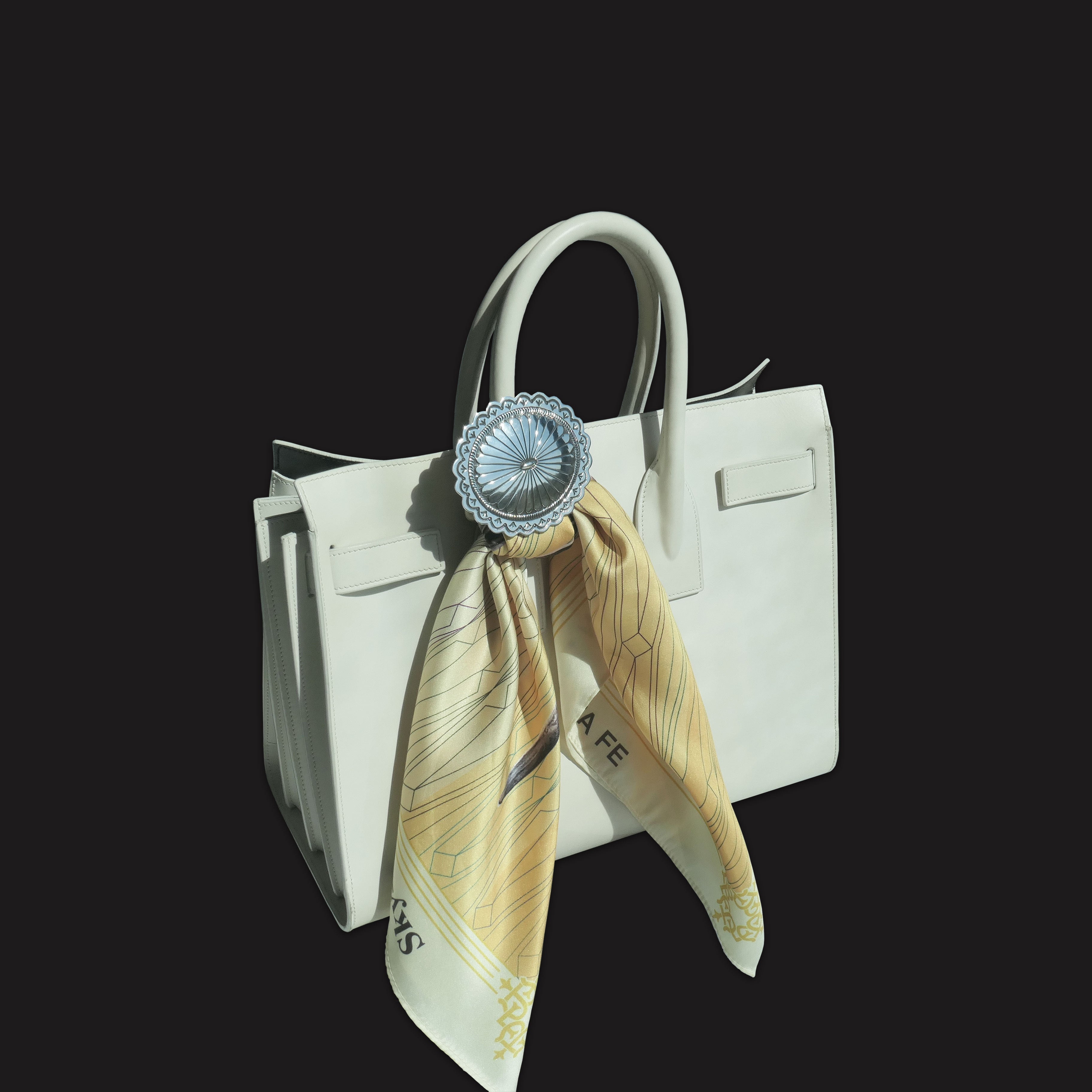 4 Corners Sterling Silver Diné concho scarf slide by Lee Charley used as a stylish handbag adornment, securing a patterned scarf to a light leather purse handle.