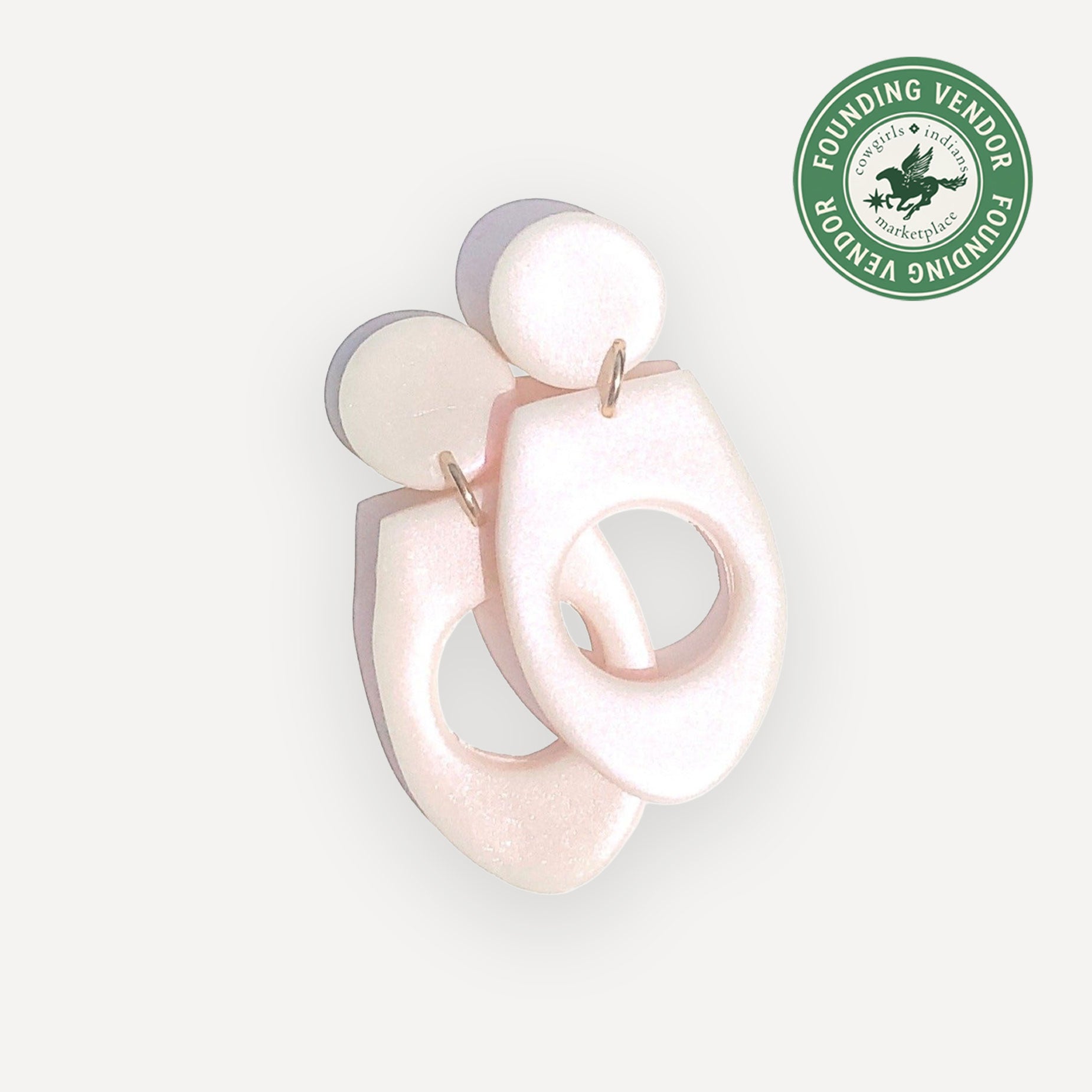 Pink abstract earrings on a light gray background with a green logo in the corner.