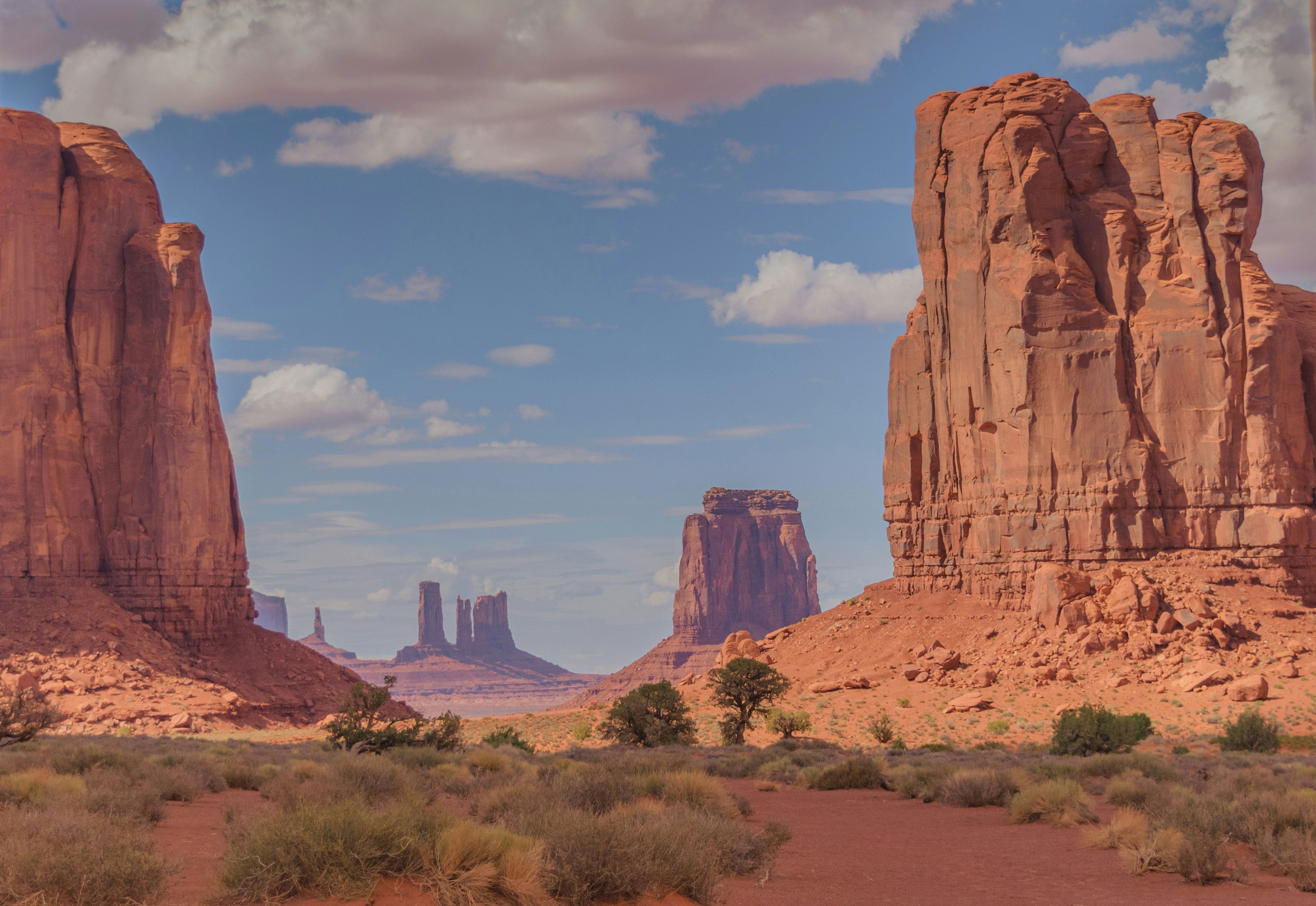 Iconic Monument Valley Navajo Tribal Park landscape featuring the famous Mittens and Merrick Butte red sandstone formations under a partly cloudy sky, Arizona/Utah border.