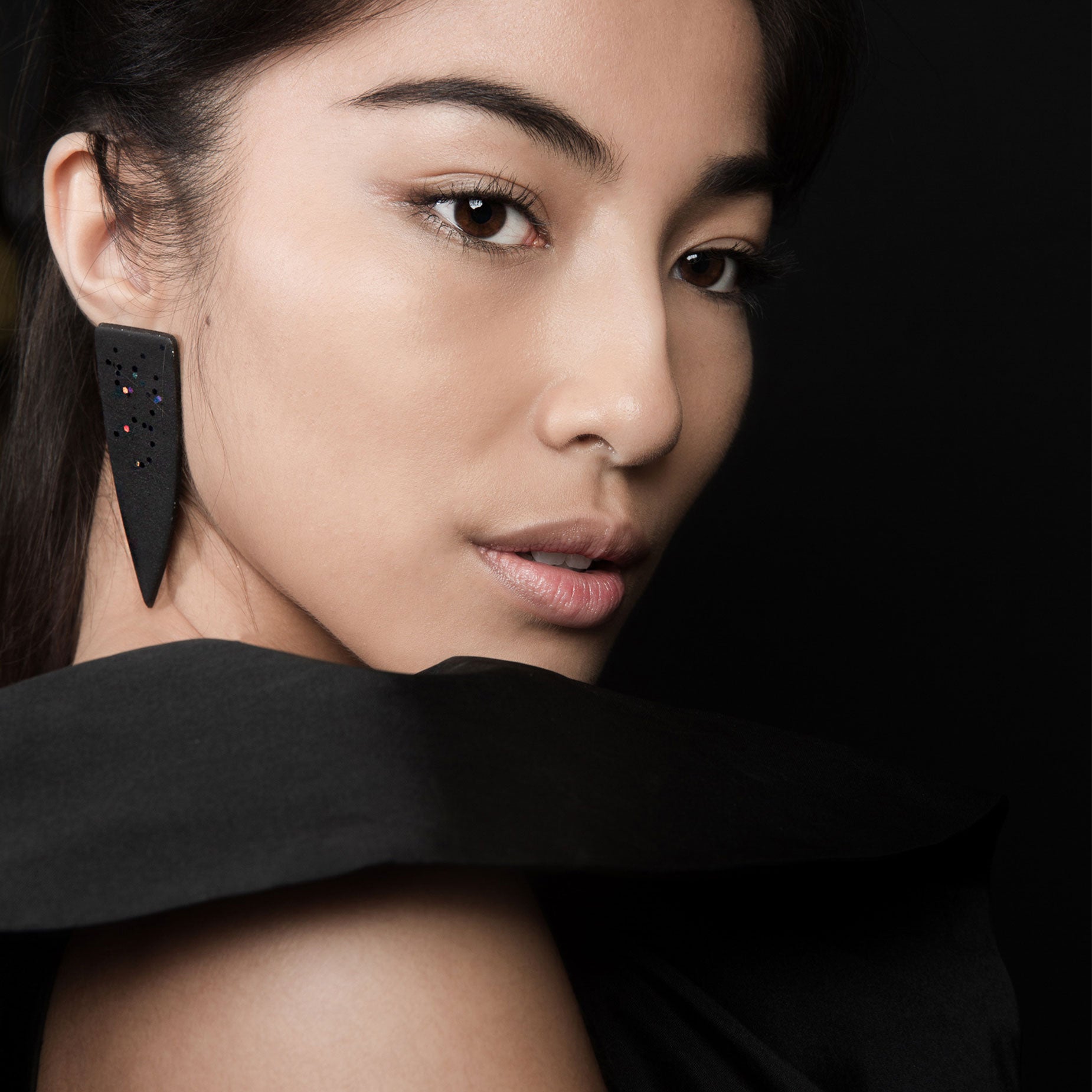 Close-up of a woman wearing a black obsidian dagger earrings against a dark background