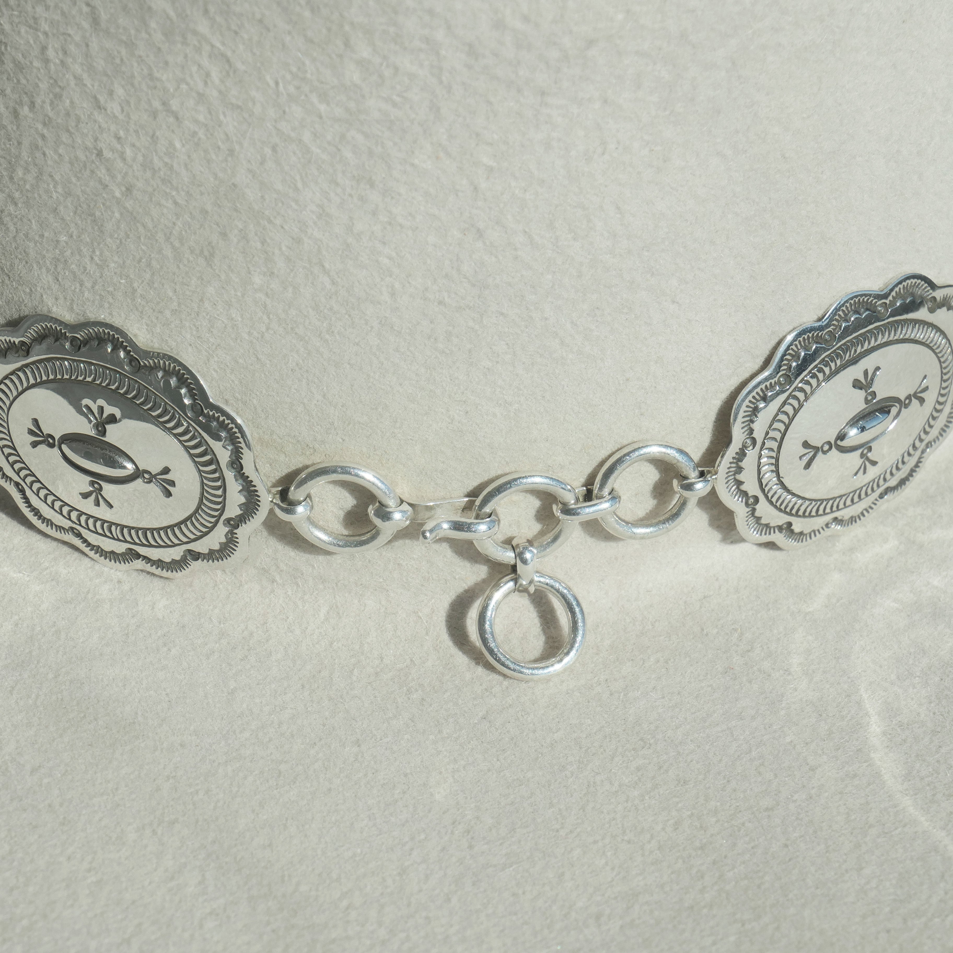 Close-up of the back fastening of the Texas Flood hatband, showing how the silver-tone oval concho chain connects using linked rings against the light colored hat fabric.