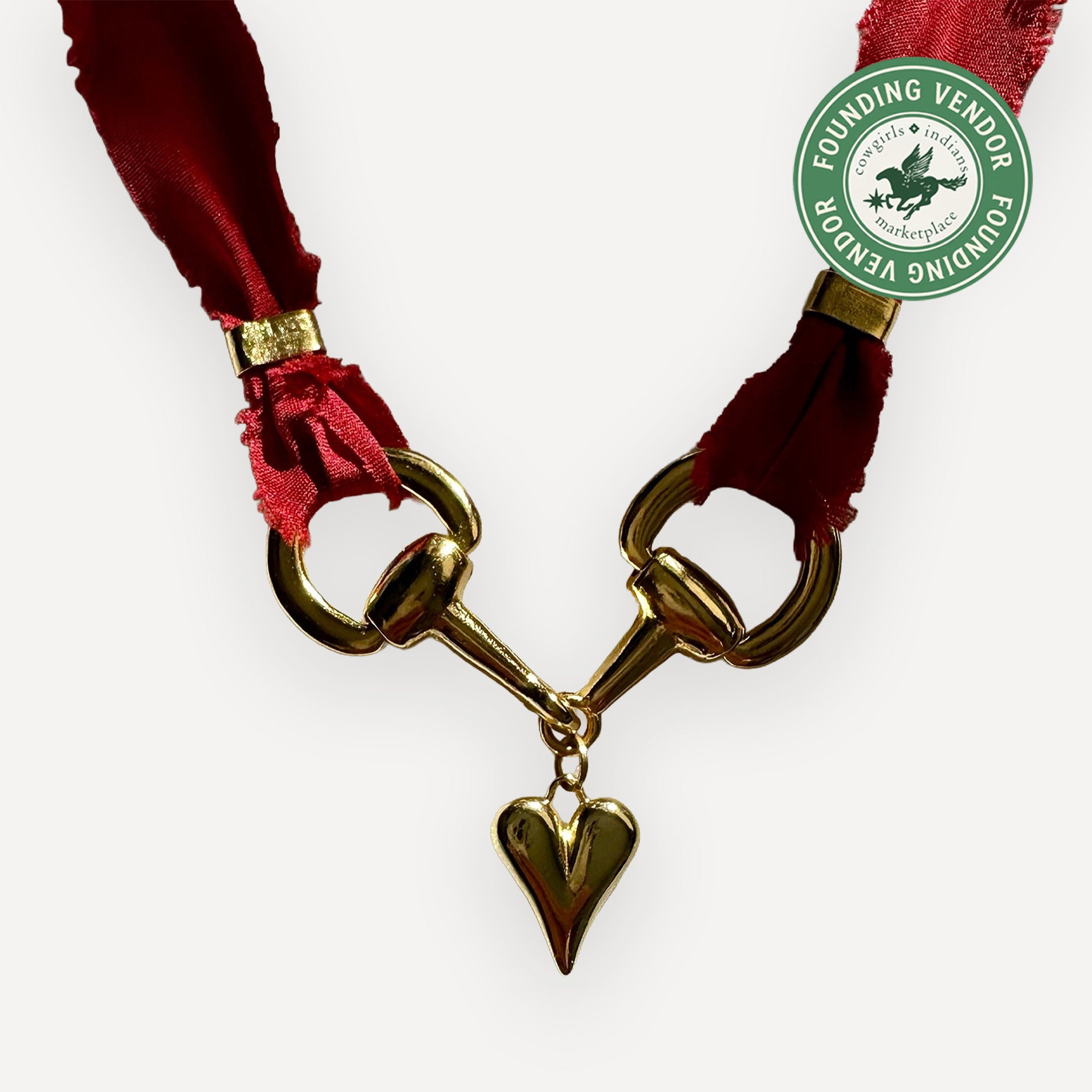 Gold bridle bit with red satin ribbon and heart pendant on a white background