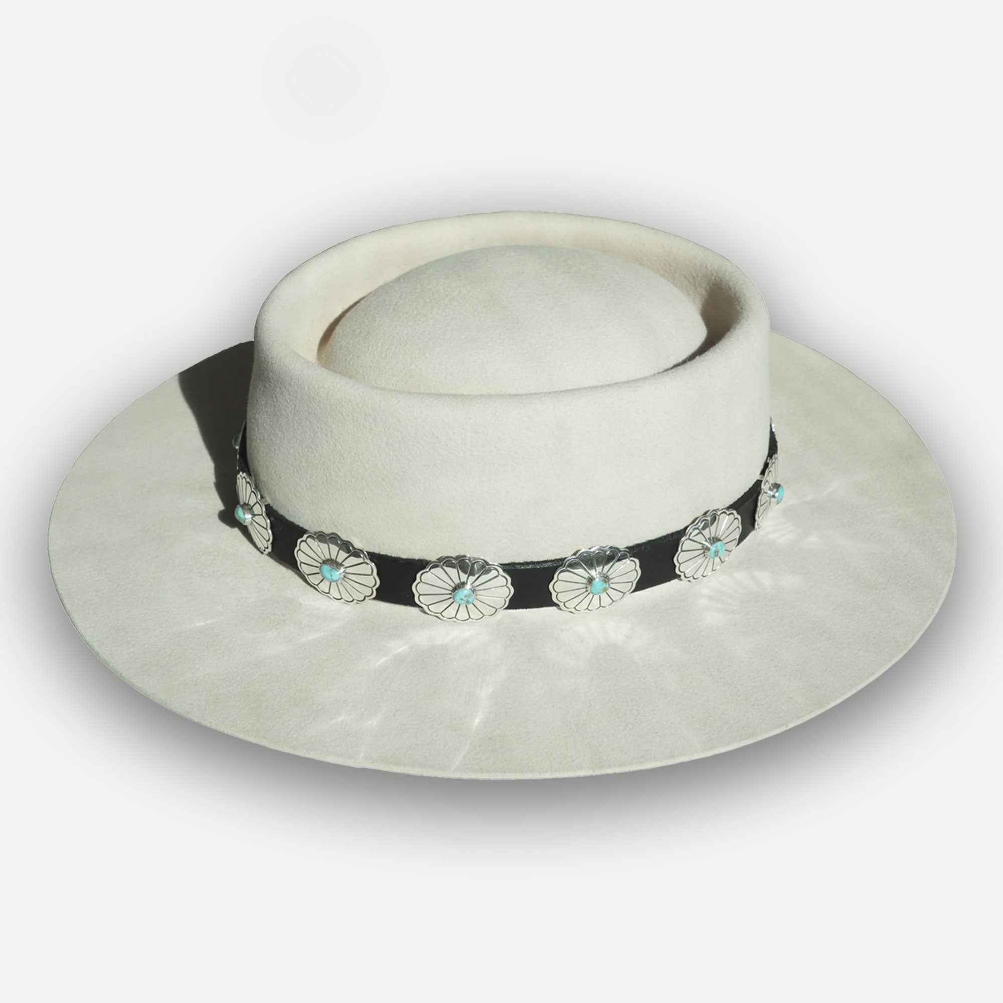 White hat with a decorative black band featuring silver and turquoise accents on a light gray background