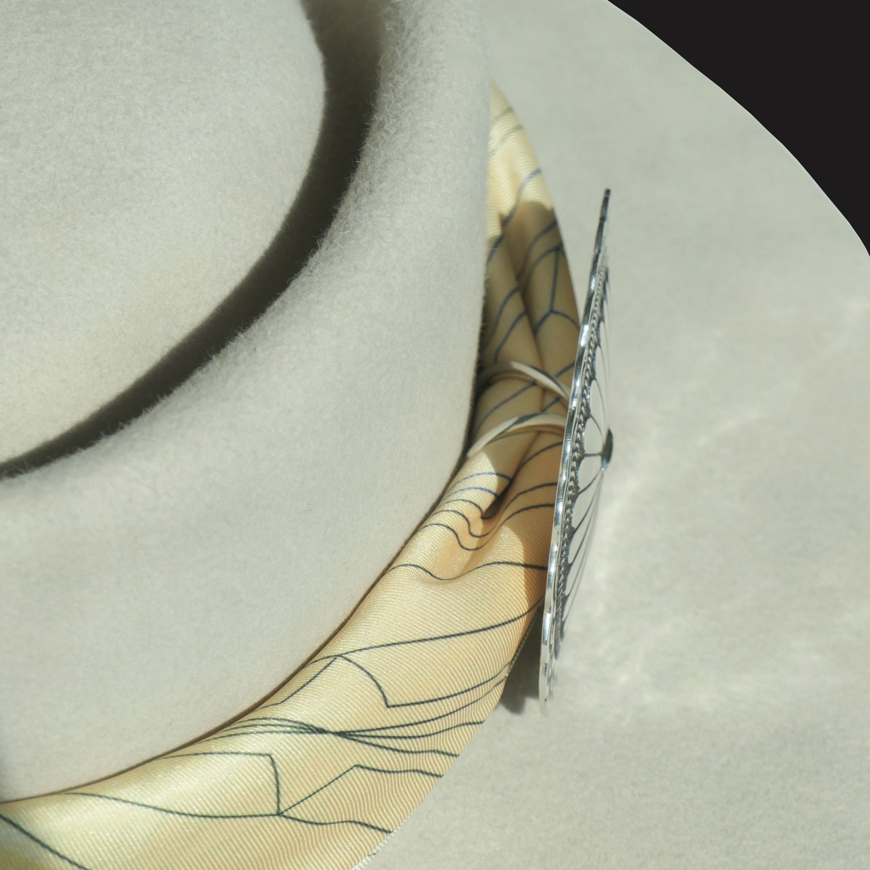 Back view of the Lee Charley 4 Corners Navajo concho scarf slide in sterling silver, showing the integrated loop or bar mechanism securing a silk scarf around a hat.