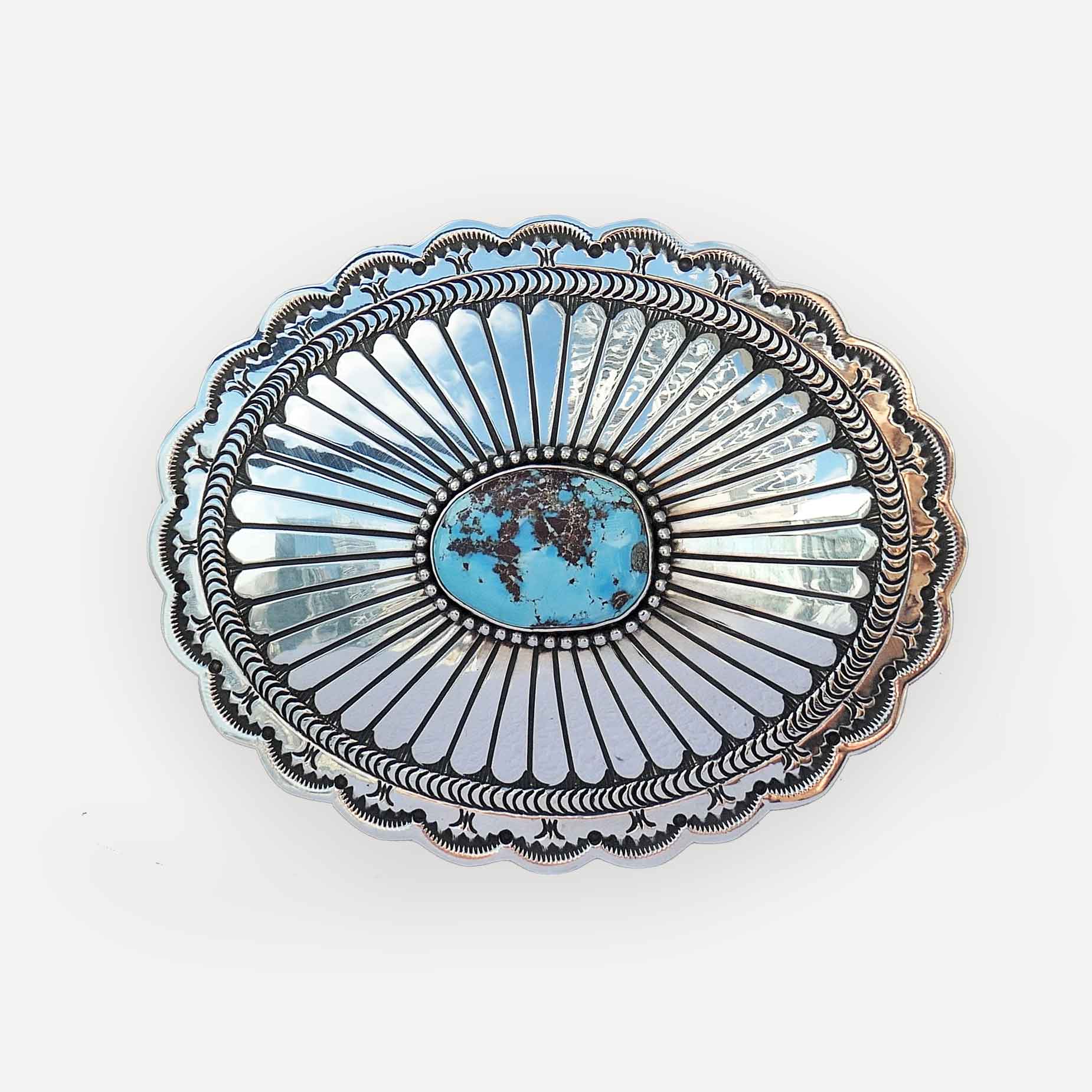 A contemporary navajo silver belt buckle featuring a central oval turquoise cabochon surrounded by radiating sunburst patterns and a scalloped decorative border.