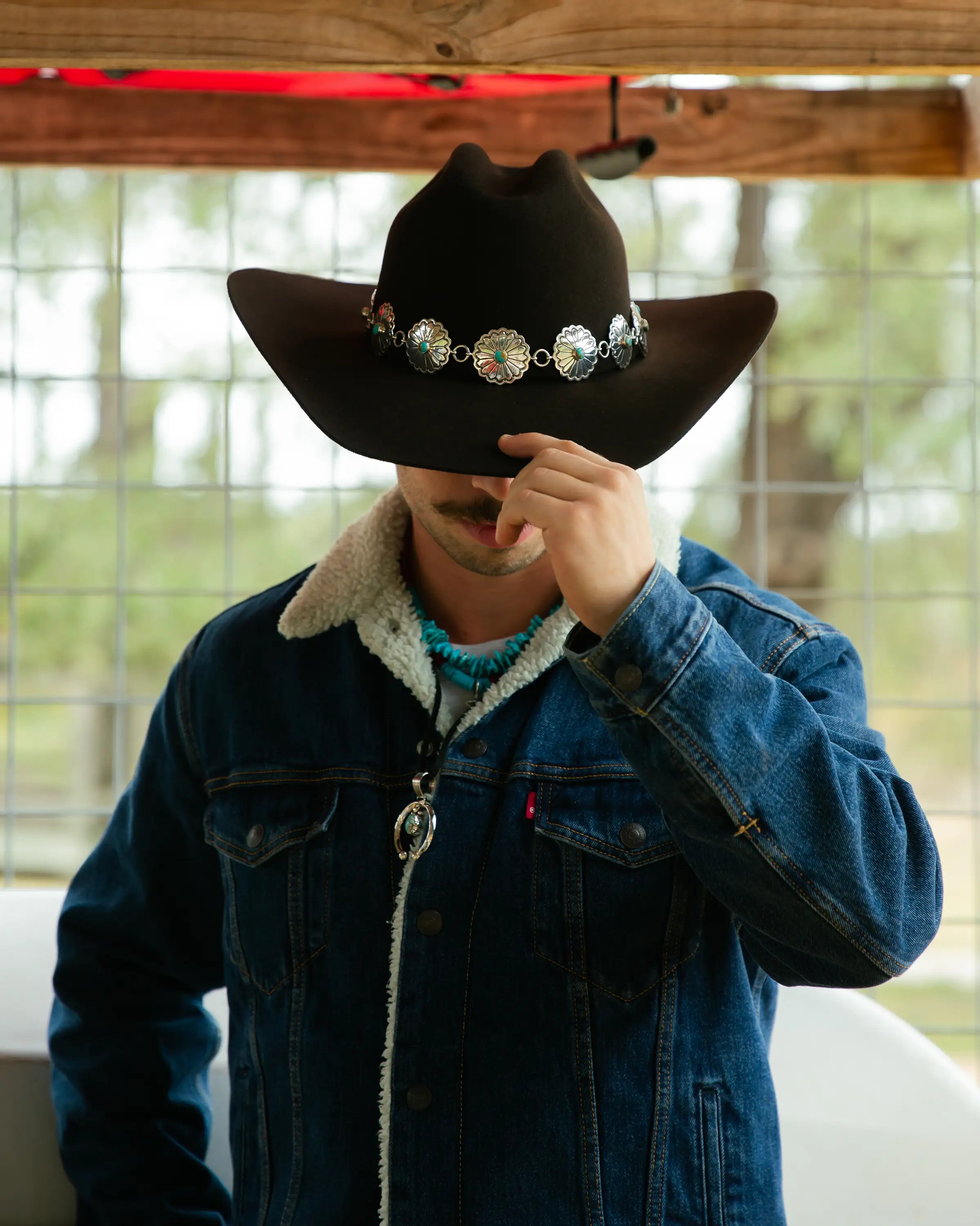 Cowboy wearing a cowboy hat with decorative sterling silver band and denim jacket in barn.