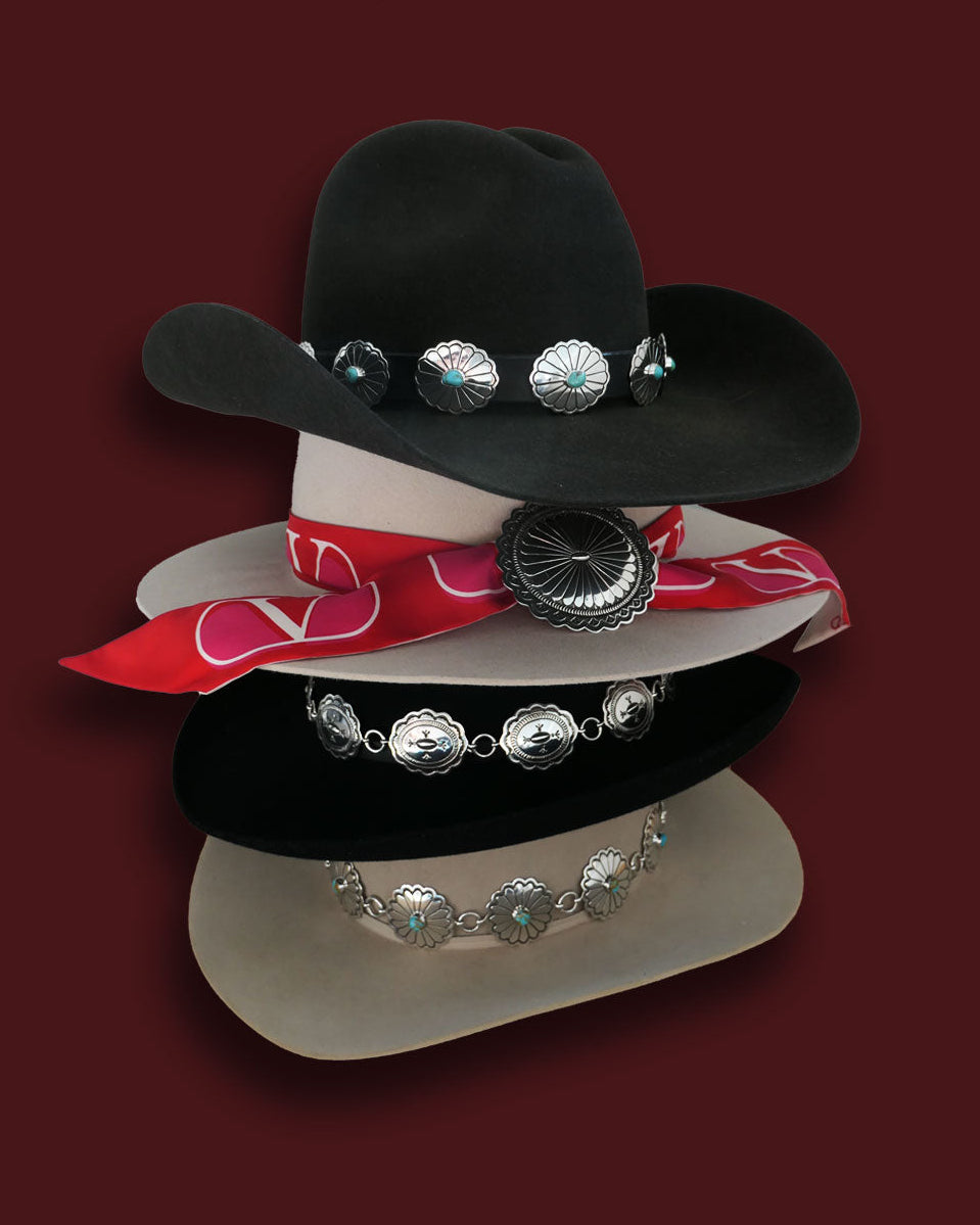 Brown, black, and silver cowboy hats stacked on each other with sterling silver hat bands. 