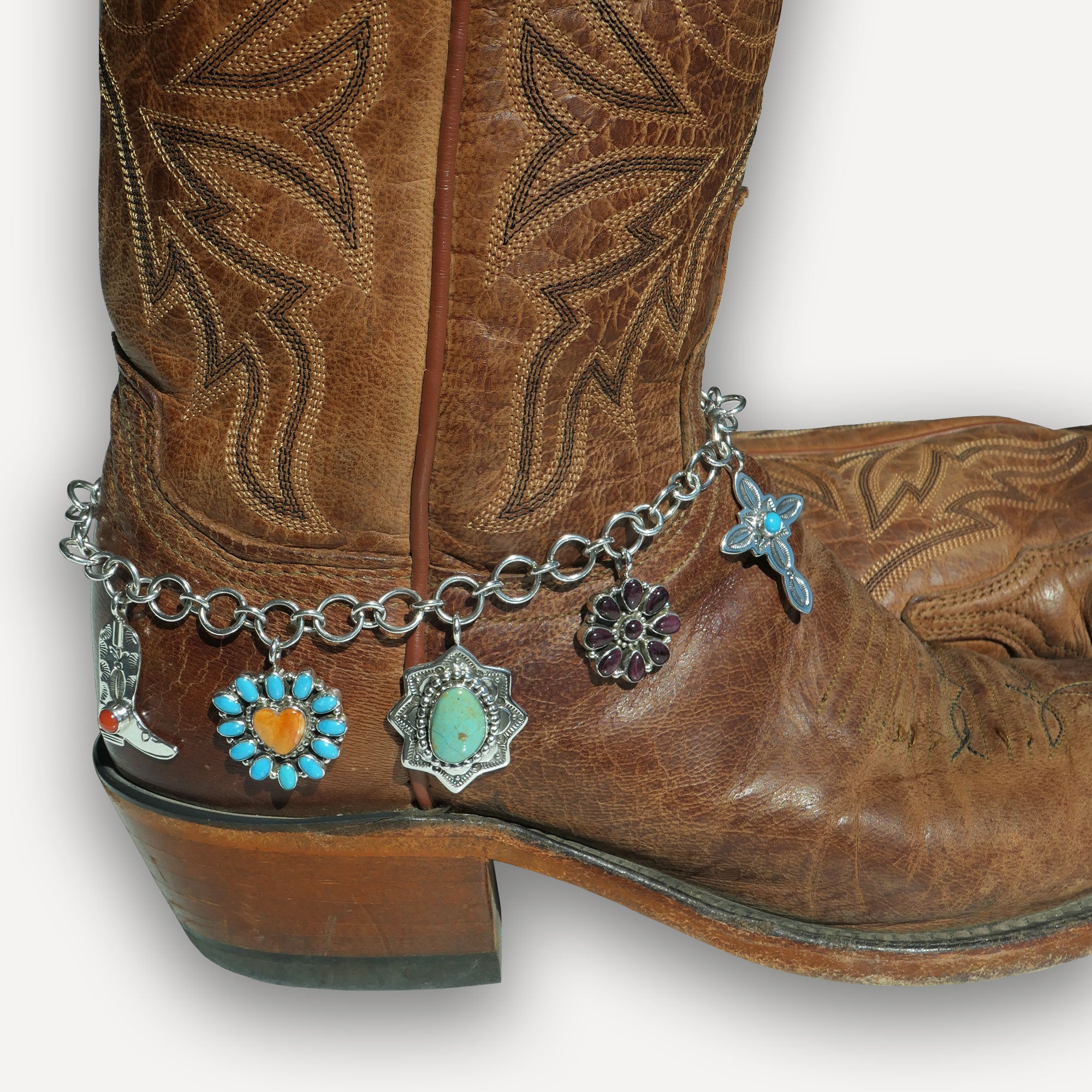 Brown cowgirl boot with a silver anklet featuring boot charms on a white background