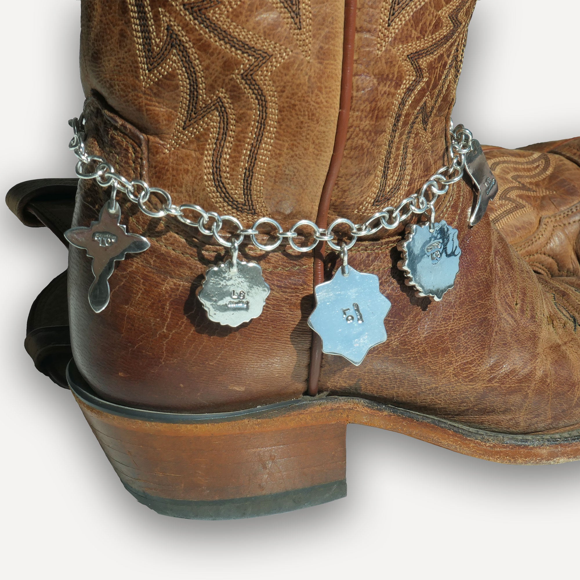 Brown cowboy boots for women with a silver chain anklet featuring charms on a white background