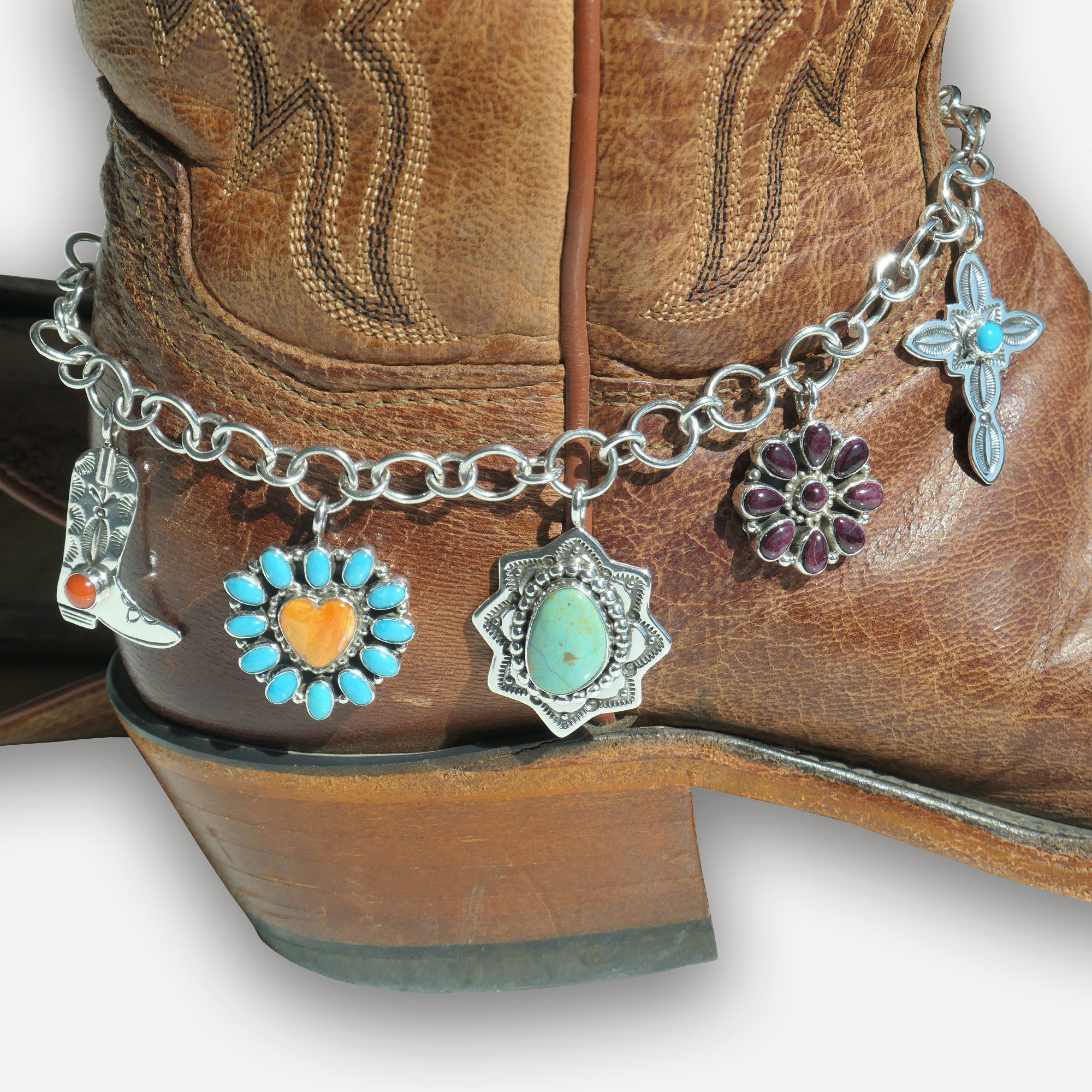 Close-up of a brown cowboy boot with a silver boot bracelet featuring various charms.