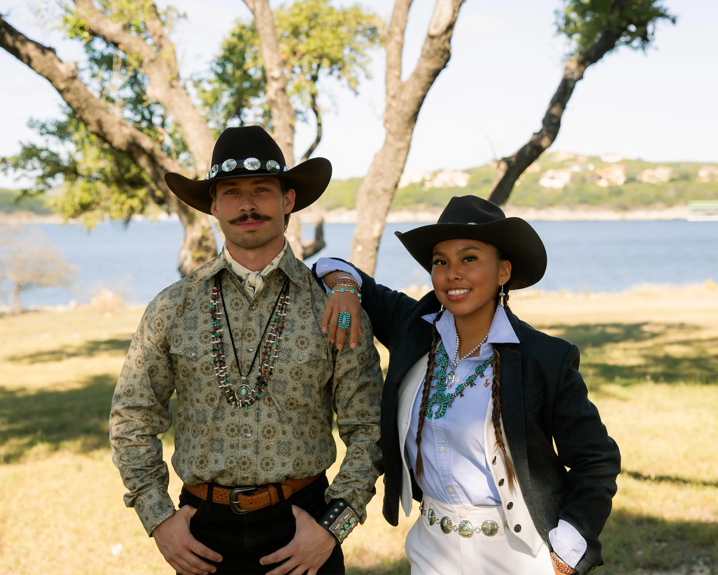 Two people in cowboy hats standing outdoors by a lake with modern Native American Jewelry 