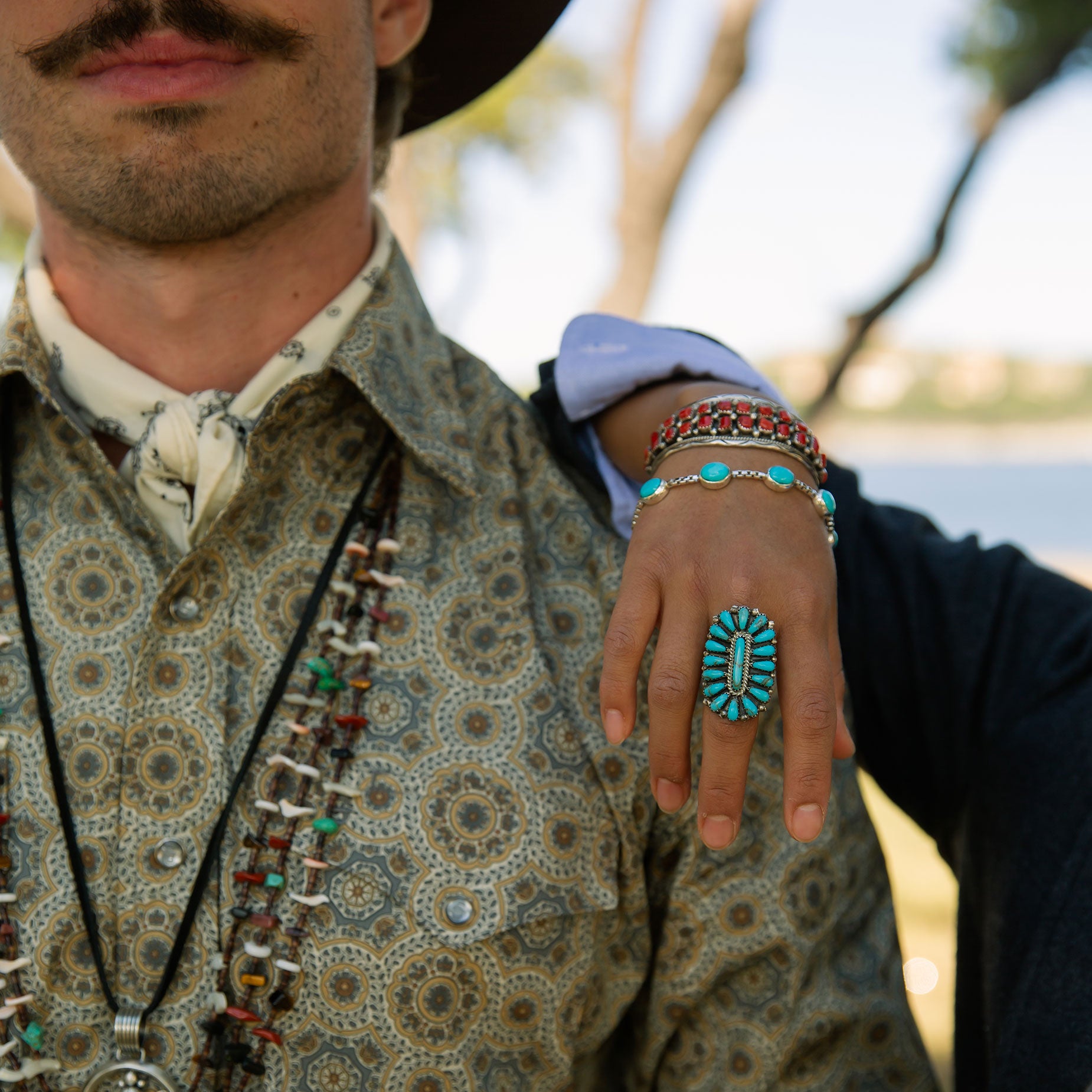 Person wearing a patterned shirt with jewelry including a cluster ring and bracelets.