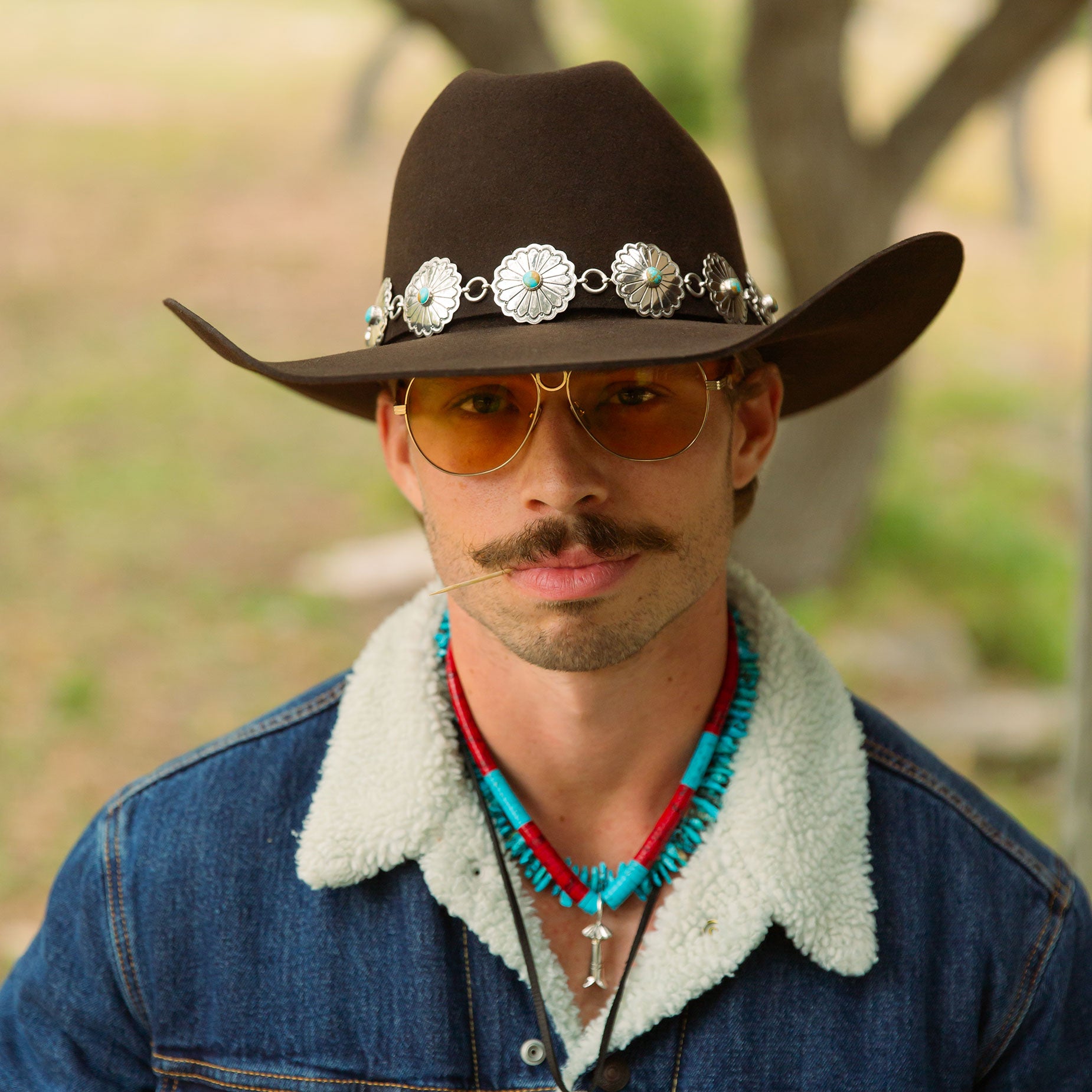 Cowboy wearing a cowboy hat with decorative band, sunglasses, and a denim jacket with fur lining.