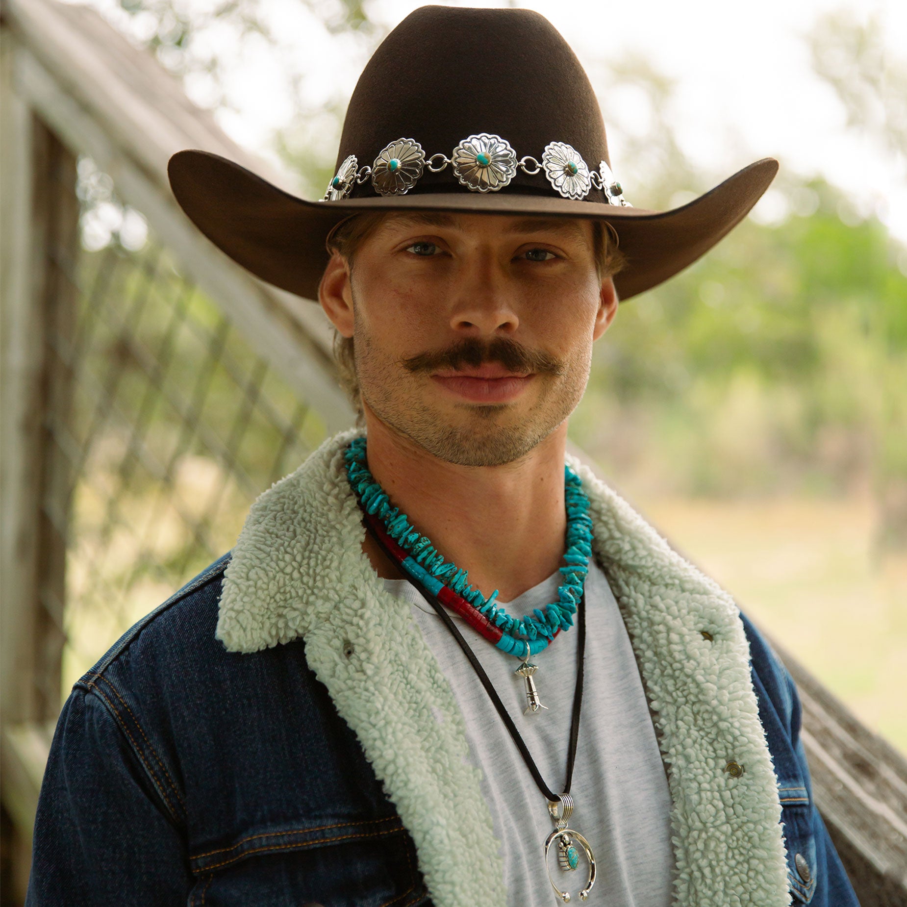 Man wearing turquoise necklaces with sterling silver navajo pendants and brown resistol cowboy hat with cowgirls & indians nizhoni hat band. 