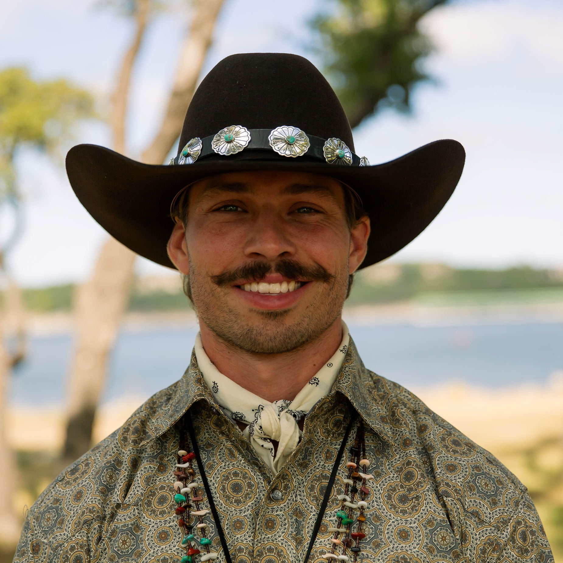 Man wearing a cowboy hat with hat band and Stetson shirt outdoors