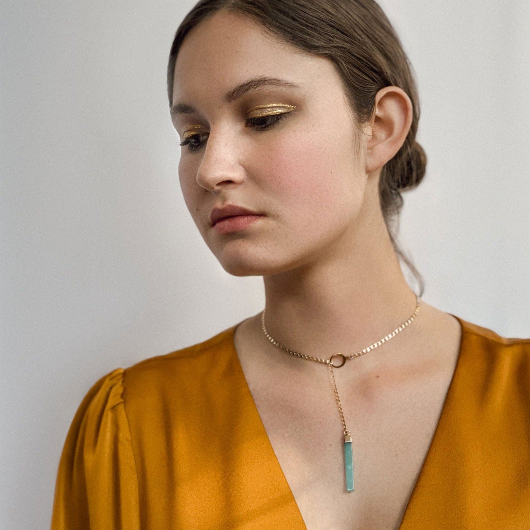 Woman wearing a gold lariat necklace with a jade pendant against a plain background