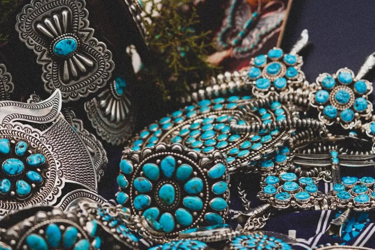 Close-up of silver and turquoise jewelry on a dark surface with a navy card in the background.
