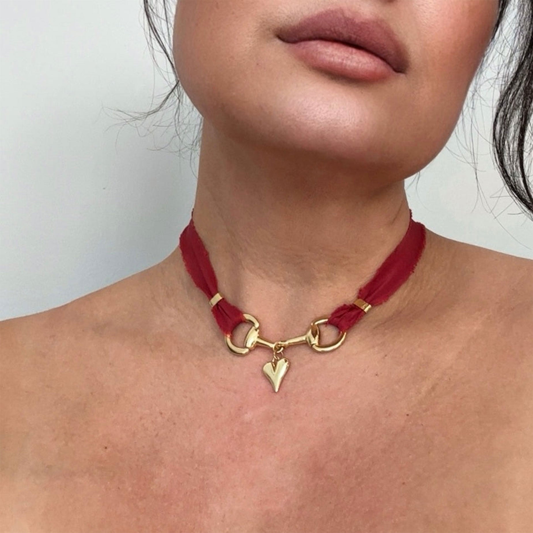 Red choker necklace with gold clasp and heart charm worn by a person.