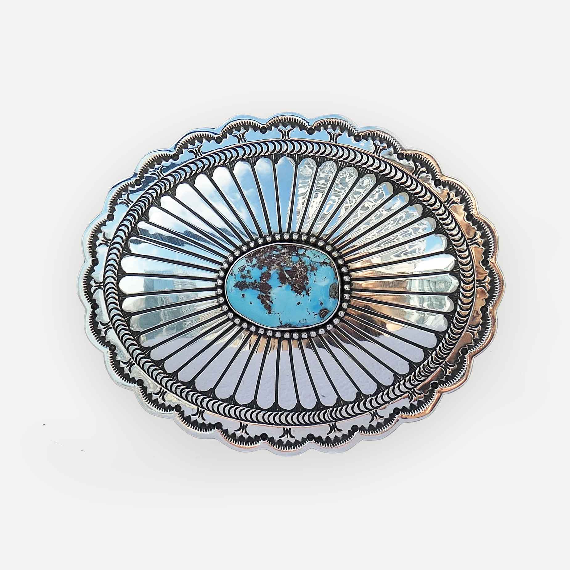 An oval sterling silver belt buckle featuring a central turquoise stone surrounded by radiating engraved metal rays and a scalloped outer border, shown on a plain white background.