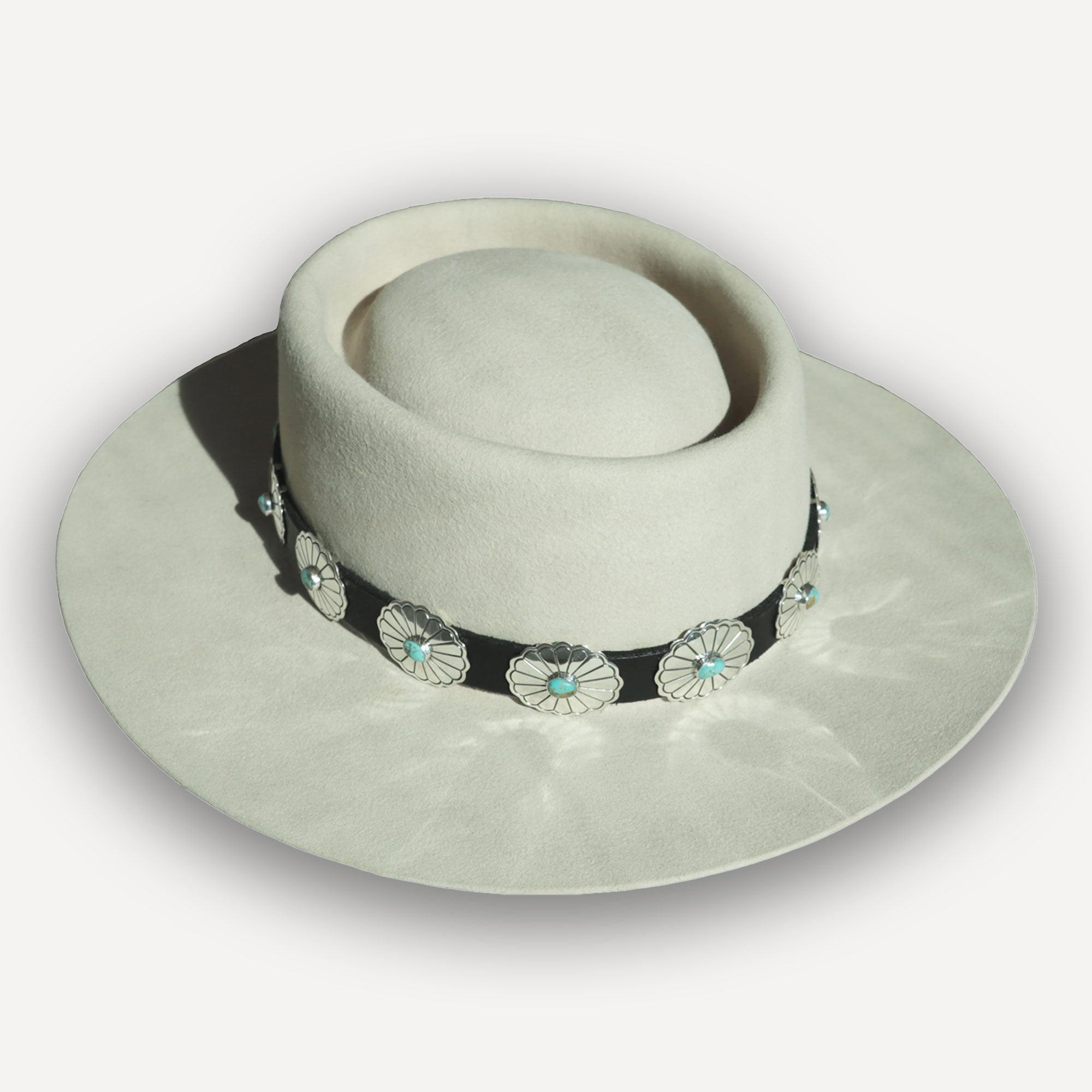 Rough Rider hat band: Stamped silver conchos with turquoise centers on a dark leather band, shown on a light felt Montana Territory Hat.