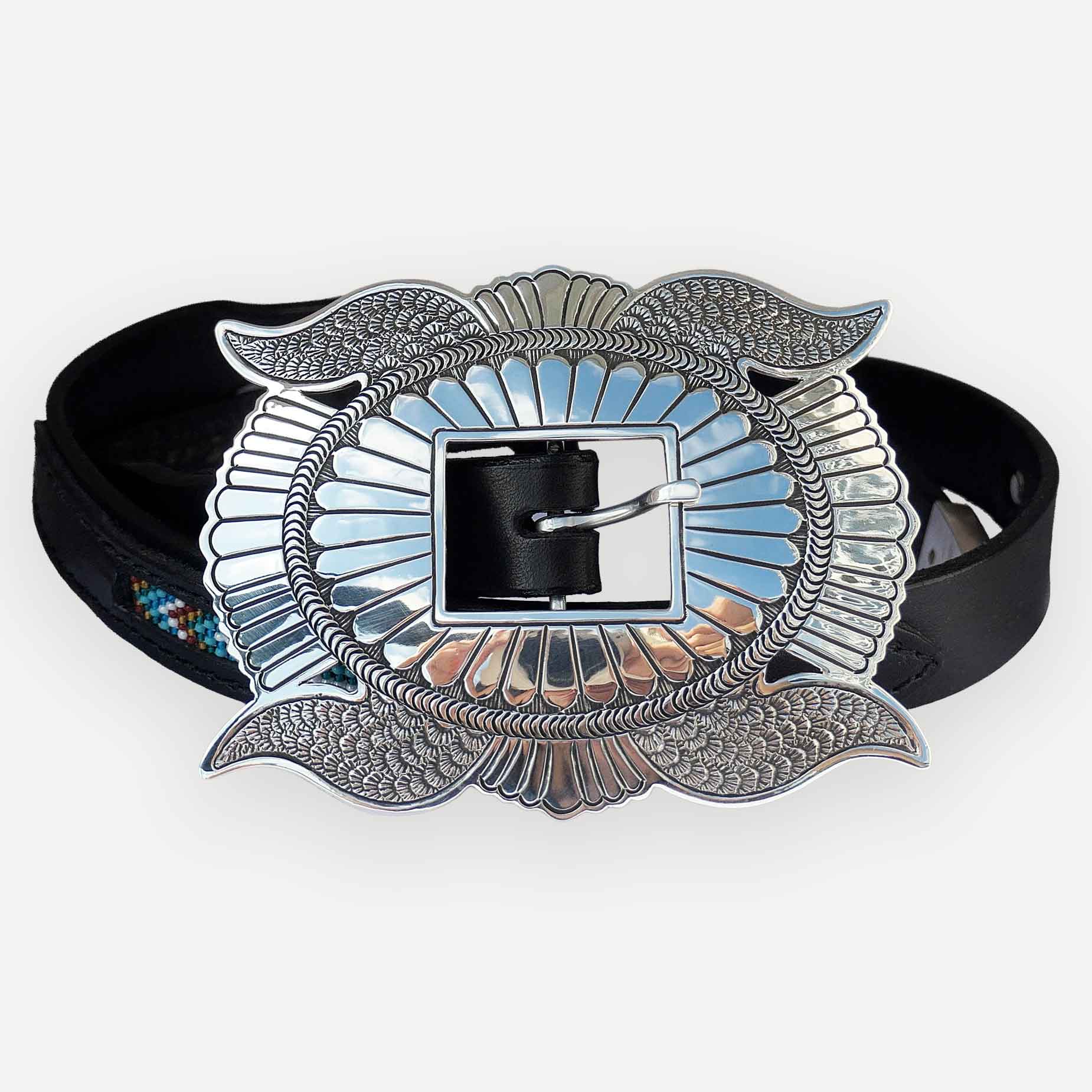 A western-style belt buckle with an ornate silver-toned winged design and a black leather strap, shown on a light gray background.