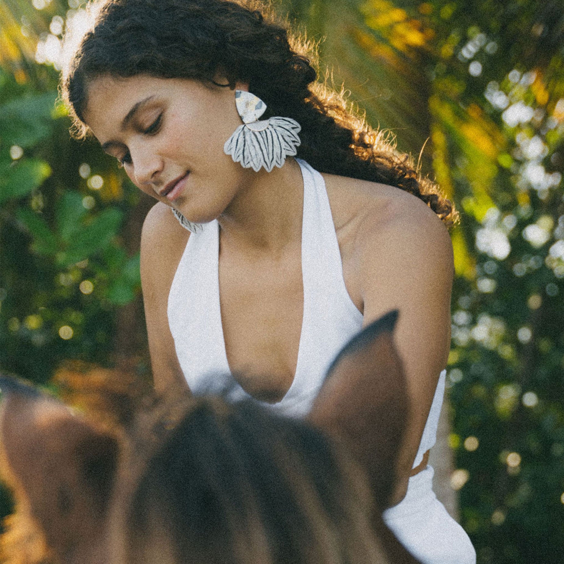 Woman wearing a white sleeveless top with floral earrings in a natural setting