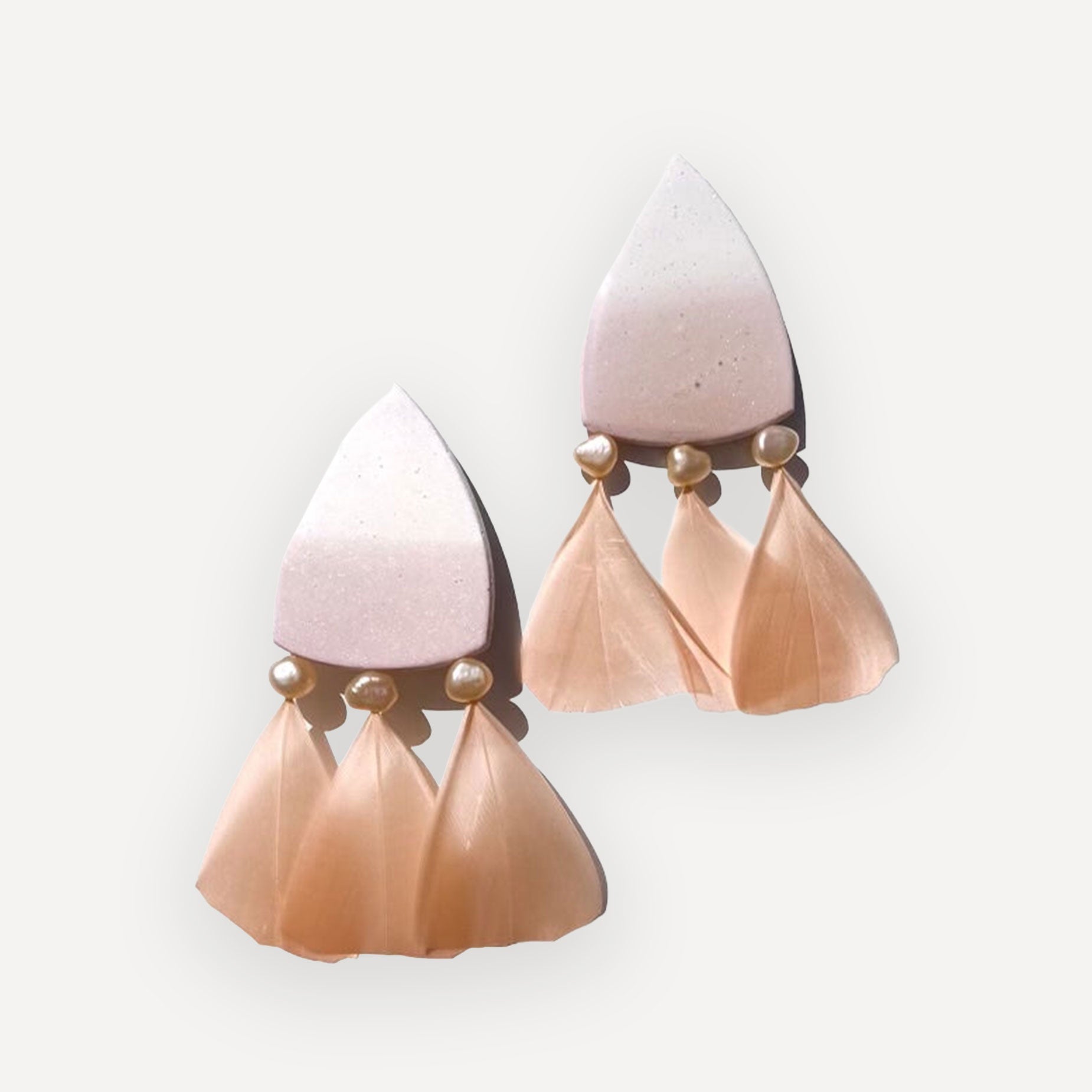 Pair of earrings with pink and beige teardrop shapes on a light gray background